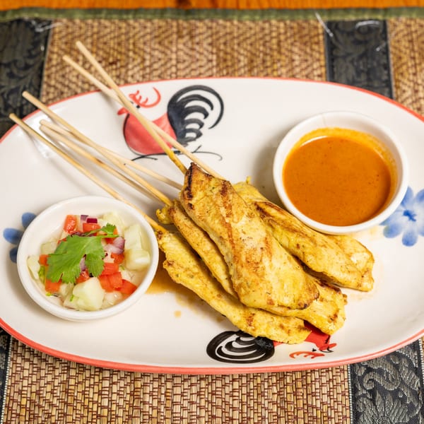Chicken satay skewers with peanut sauce and cucumber relish on a decorative plate.