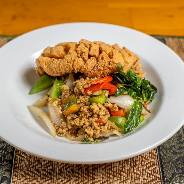 Crispy fried fish over ground meat, bell peppers, onions, and basil on a white plate.