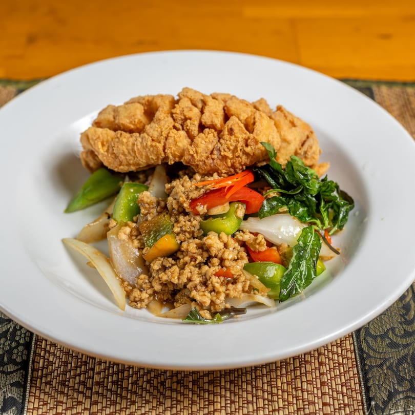 Crispy fried fish over ground meat, bell peppers, onions, and basil on a white plate.