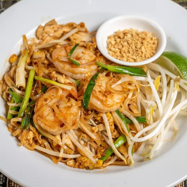 Shrimp Pad Thai with noodles, bean sprouts, green onions, and a side of crushed peanuts.