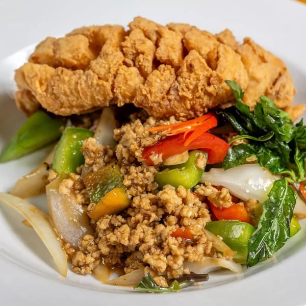 Crispy fried fish fillet with stir-fried ground chicken, bell peppers, onions, and basil on a white plate.