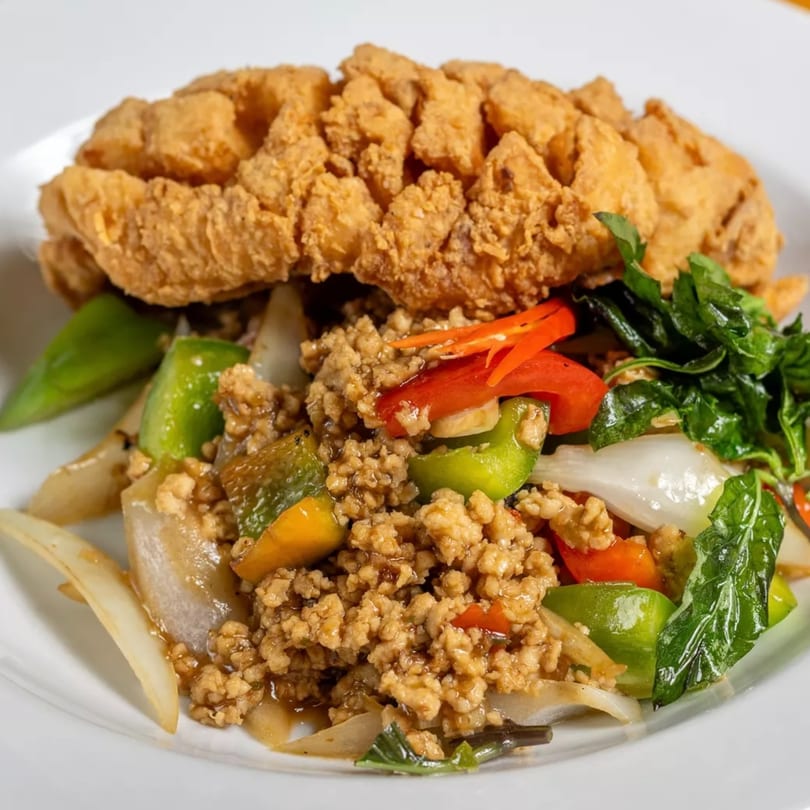 Crispy fried fish fillet with stir-fried ground chicken, bell peppers, onions, and basil on a white plate.