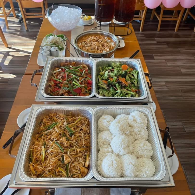 A buffet table with various Thai dishes, including noodles, rice, stir-fry, and curry.
