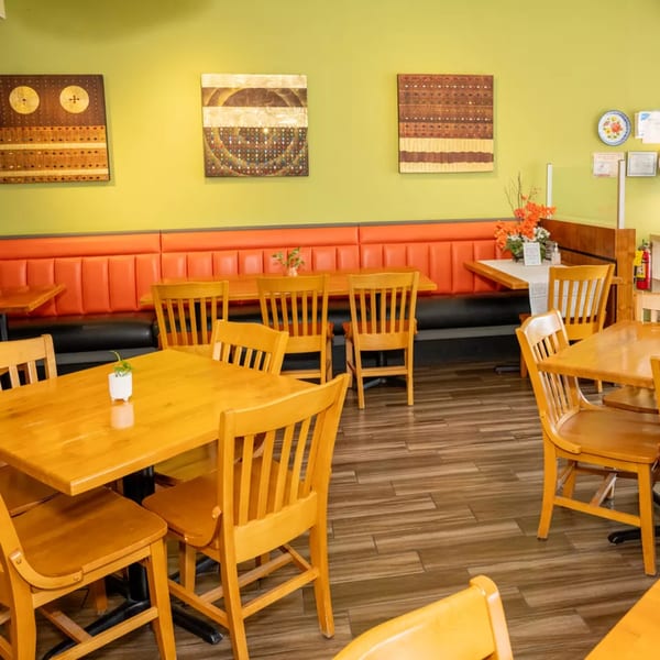 Restaurant interior with wooden tables and chairs, orange booth seating, and lime green walls with artwork.