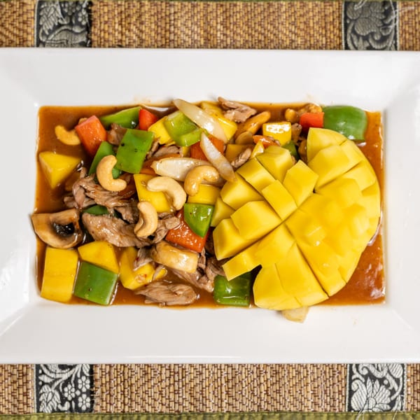 Mango chicken stir-fry with bell peppers, cashews, and mushrooms on a white rectangular plate.