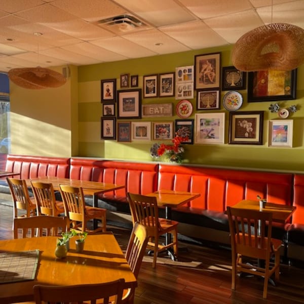 Restaurant interior with red booth seating, wooden tables, chairs, and a gallery wall with diverse art.