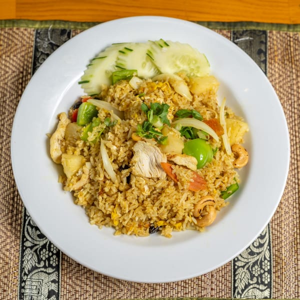 Pineapple fried rice with chicken, cashews, vegetables, and cucumber slices on a white plate.